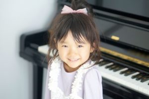 ピアノの前で恥ずかしそうに微笑む幼稚園の女の子の写真