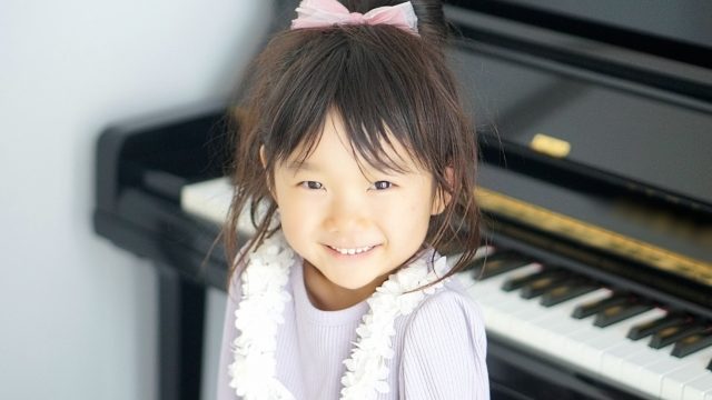 ピアノの前で恥ずかしそうに微笑む幼稚園の女の子の写真