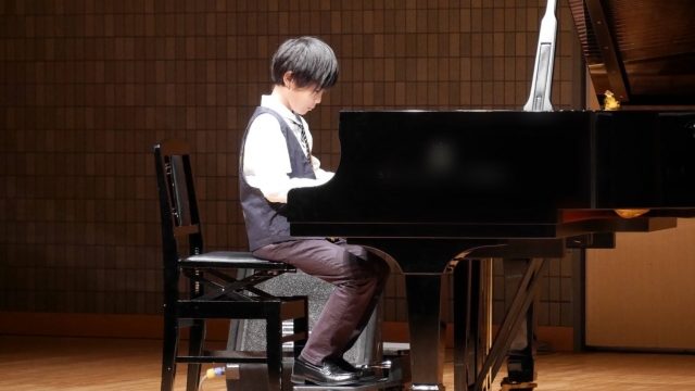 ピアノコンクールで補助ペダルを使って演奏する男の子の写真